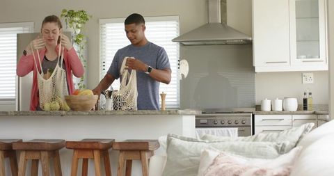 Couple unpacking fruit into reusable mesh bags on granite kitchen island modern lifestyle