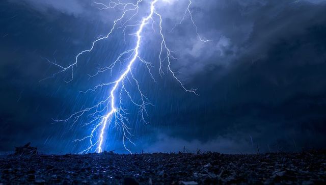 Branched Lightning Bolt Striking Rain-Soaked Plain Under Dark Storm Clouds at Night