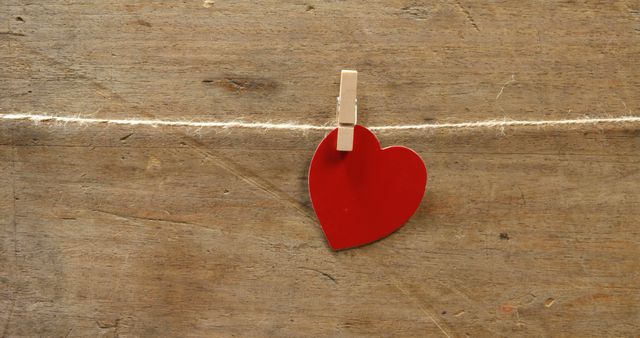 A red heart hangs from a clothespin attached to a string against a wooden background, with copy space. It symbolizes love, affection, and the concept of hanging one's heart out for someone.