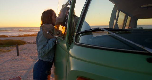 Couple enjoying a romantic moment at the beach as the sun sets, leaning on a vintage van. Perfect for use in lifestyle blogs, romantic greeting cards, travel websites, and advertisement campaigns evoking feelings of adventure and love.
