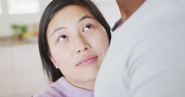 Woman with gentle expression looking up while in close embrace indoors. Warm moment showcasing affection and emotional connection. Ideal for themes of love, relationship counseling, emotional well-being, interpersonal intimacy, and human connection.