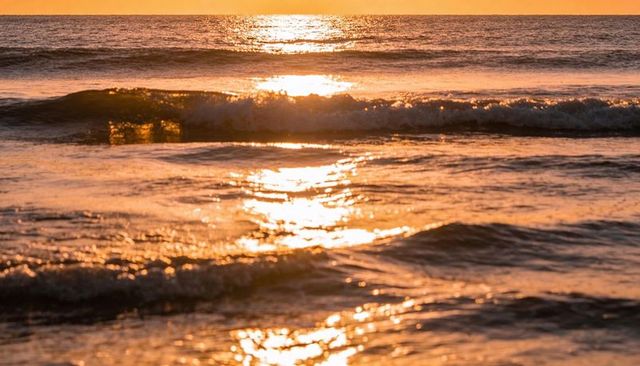 Glittering ocean reflecting golden sunset light with breaking waves and soft foam