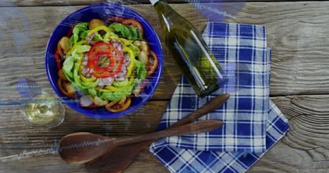 Rustic summer salad in cobalt bowl with white wine and wooden servers on weathered wood