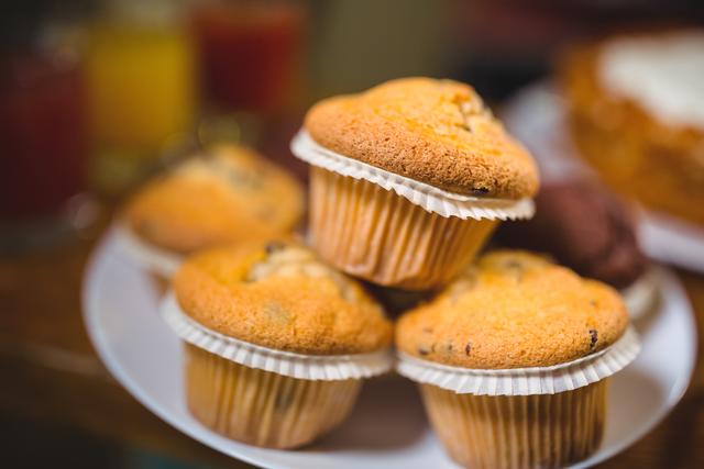 Freshly baked muffins stacked on a plate in a cozy café. Ideal for use in food blogs, bakery advertisements, café menus, and social media posts promoting baked goods and desserts.