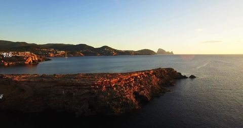 Rocky headland glowing at sunset with calm sea, distant hillside villas, coastal panorama