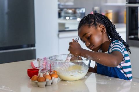 African girl mixing cake batter at kitchen island wearing blue apron and striped shirt