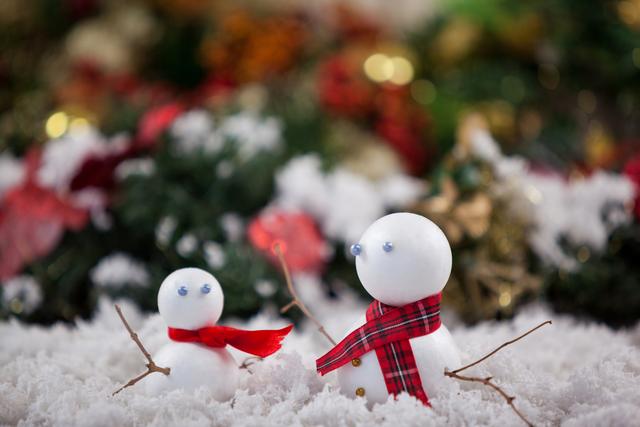 Two snowmen with red and plaid scarves sitting in snow with festive background. Ideal for holiday cards, winter-themed decorations, Christmas promotions, and seasonal advertisements.