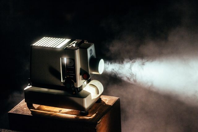 This image shows a vintage film projector casting a beam of light in a dark, misty environment. The scene exudes a nostalgic, retro vibe, making it perfect for use in film industry-related marketing materials, retro-themed projects, or vintage cinema articles.