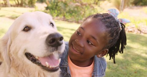 Young girl gently petting happy dog in sunny park