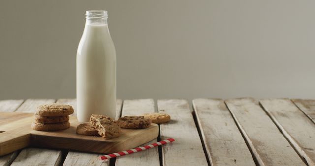 Fresh glass bottle of milk next to stacked chocolate chip cookies on rustic wooden table implies wholesome and nostalgia-filled snack time. Suitable for use in marketing materials for dairies, bakeries, or rustic-themed cafes. Ideal for articles on healthy snacks, vintage scenery, or dessert recipes.