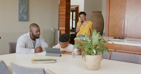 African American family sitting at kitchen table using tablet while mother talking on phone