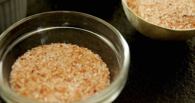 Pink Himalayan salt displayed in glass and wooden bowls, showcasing its distinct color and crystalline texture. This image is perfect for use in culinary articles, health and wellness blogs, cooking websites, or food product advertisements highlighting natural and organic ingredients.