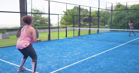 African american women playing padel on blue outdoor court, fitness and fun