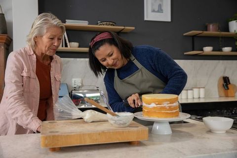 Mature women decorating layered cake in home kitchen, frosting workshop and mentoring