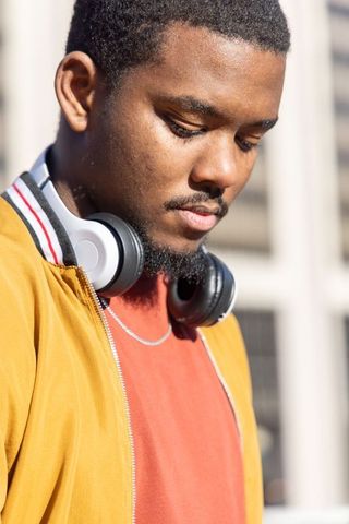 Contemplative african american man wearing headphones and mustard jacket in urban sunlight