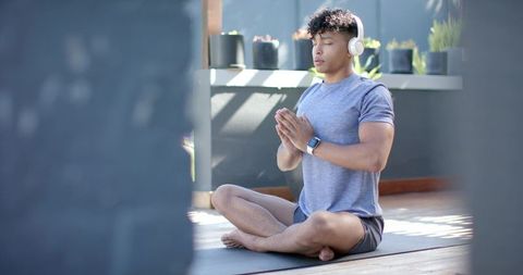 African american man meditating on terrace with headphones and smartwatch in morning light