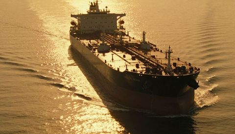 Golden-hour crude oil tanker sailing coastal waters, deck pipelines and shimmering wake