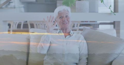 Senior Woman Waving in Bright Living Room with Natural Light