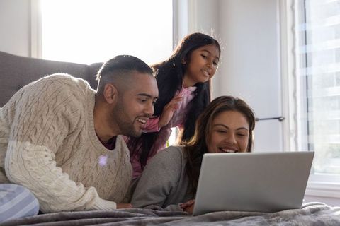 Family enjoying cozy morning browsing laptop together on bed with warm daylight