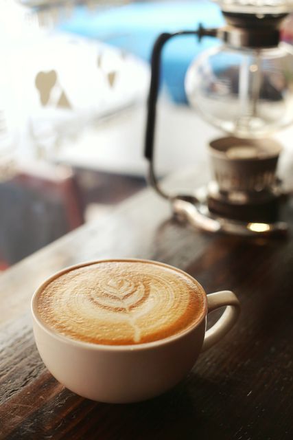 Close-up showing a beautifully crafted latte with intricate latte art on wooden counter in coffee shop. Ideal for use in marketing materials for cafes and coffee shops, coffee product advertisements, barista training manuals, and social media posts about gourmet coffee.