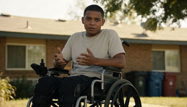 Young man in wheelchair gesturing while speaking on suburban lawn, accessible living concept