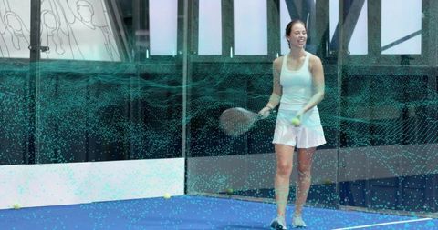 Woman practicing padel on indoor glass court holding paddle and ball, active training