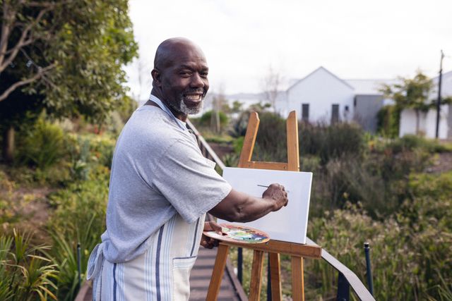 Image of happy african american man painting in garden. Lifestyle, hobby, spending free time at home and garden concept.