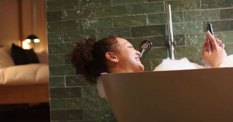 Relaxing in bubble bath scrolling smartphone in modern ensuite bedroom ambience