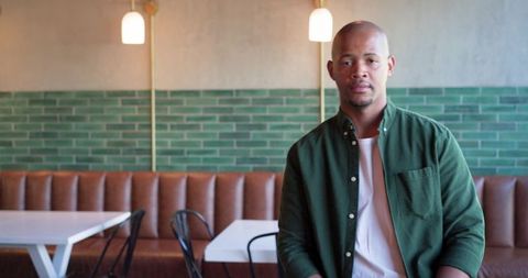 Man sitting in modern cafe booth looking at camera with green tile wall