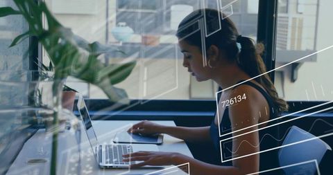 Focused woman typing on laptop by window with tablet and plant for productivity