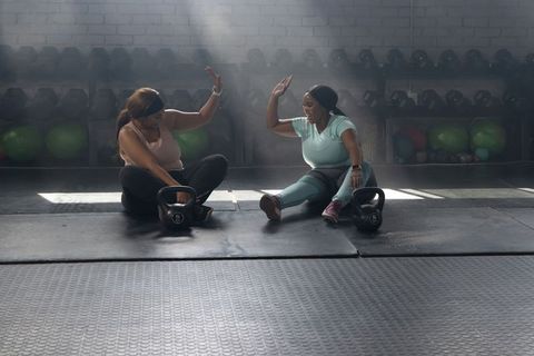 African american women working out, high-fiving after kettlebell training in gym