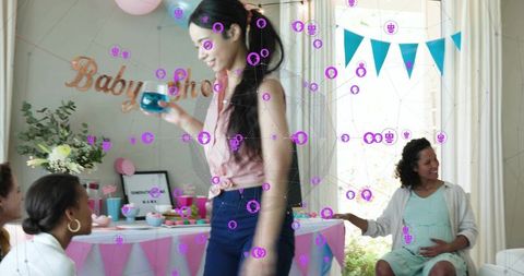 Friends celebrating baby shower at home with pregnant guest, woman walking with cup, pastel decor