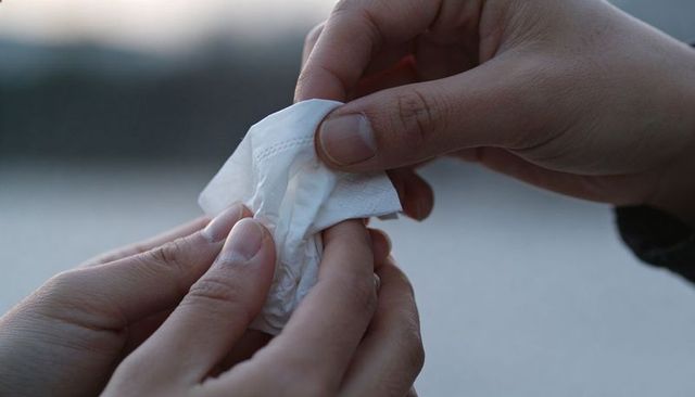 Hands passing crumpled tissue near coastal shoreline in soft overcast light