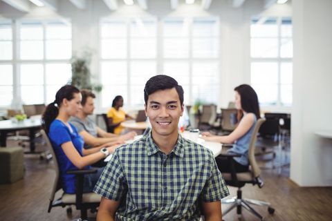 Smiling Businessman in Office with Colleagues in Background - Download Free Stock Images Pikwizard.com