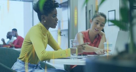 Two women collaborating over laptop and documents, planning project in modern coworking cafe