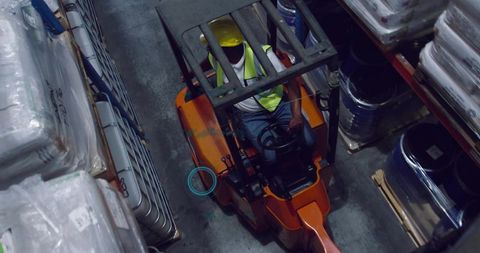 Forklift operator navigating warehouse aisle, operating controls and moving pallets
