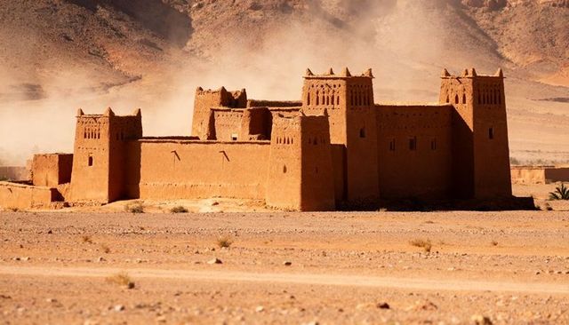 Sunlit mud-brick kasbah dominating arid plain with crenellated towers and dust haze