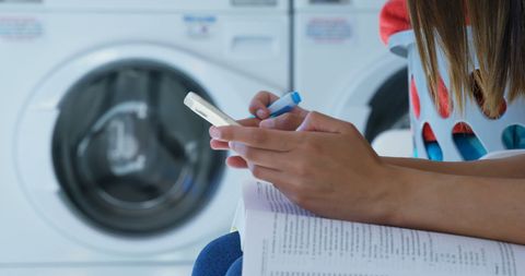 Woman Multitasking in Laundromat with Smartphone and Notebook