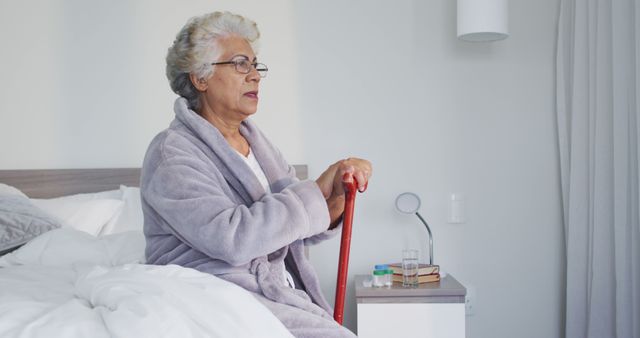 Thoughtful african american senior woman holding walking stick sitting on the bed at home. retirement senior lifestyle living in quarantine lockdown concept