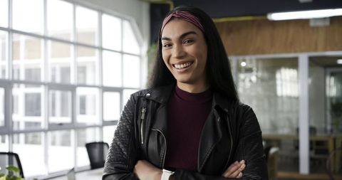 Confident asian woman standing with arms crossed smiling in modern coworking office