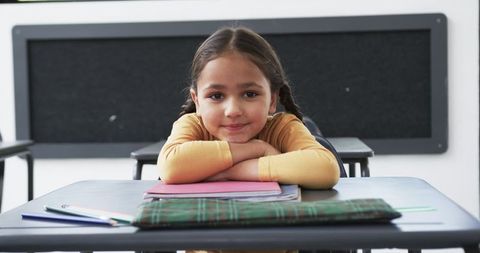 Smiling schoolgirl in classroom with notebooks