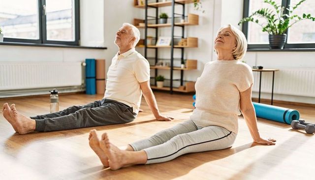 Senior couple stretching together in sunlit home studio for mobility and fitness