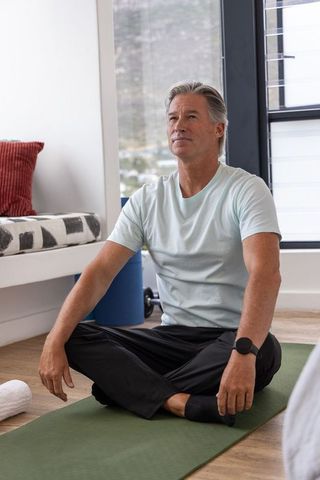 Mature man practicing mindful stretching on green mat in bright home yoga corner