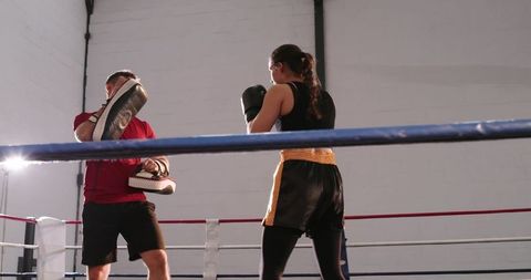 Female boxer punching while coach holding pads in boxing ring training session