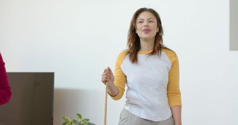 Woman cleaning living room holding broom smiling in bright minimalist interior