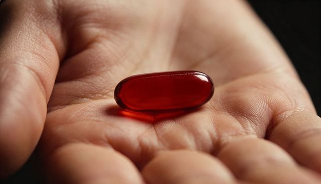 Holding red softgel capsule in open palm closeup, glossy translucent gelcap reflecting light
