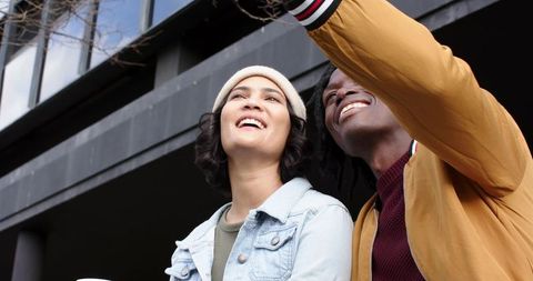 Smiling couple looking upward in urban plaza wearing denim and mustard jackets