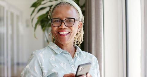 Smiling Senior Woman with Smartphone by Window