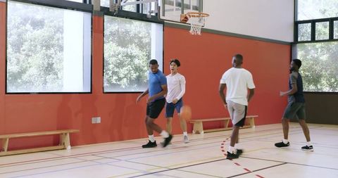 Young men playing pickup basketball in indoor gym, sprinting and passing toward hoop