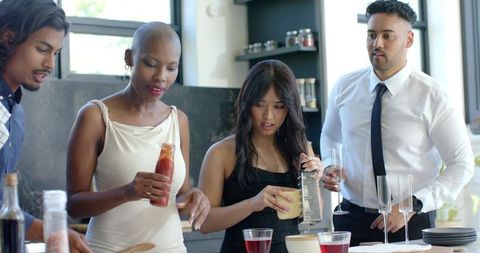 Diverse friends cooking at kitchen island preparing sauce, grating citrus, toasting